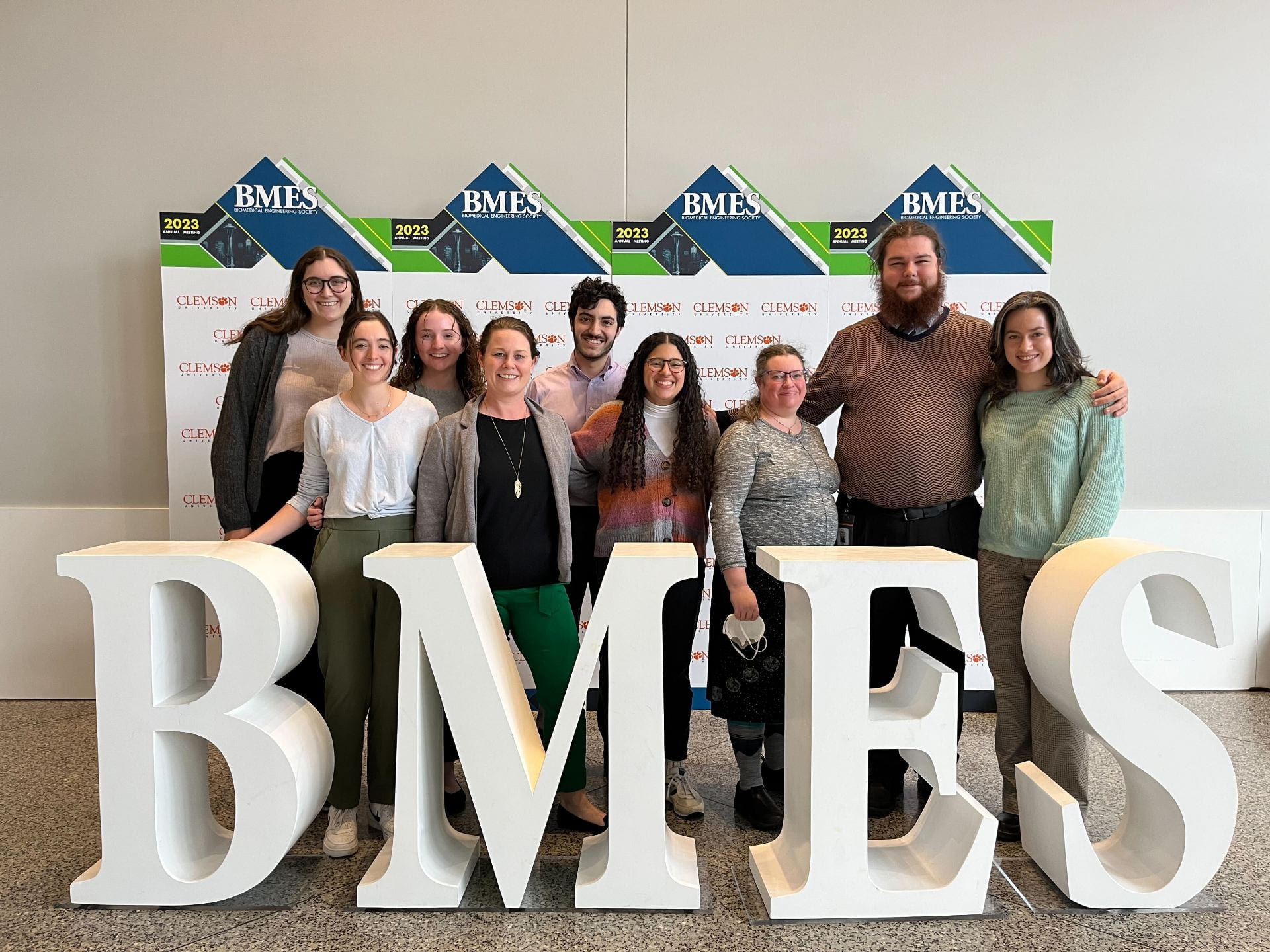 A group of people smiling behind large letters that spell out "BMES"