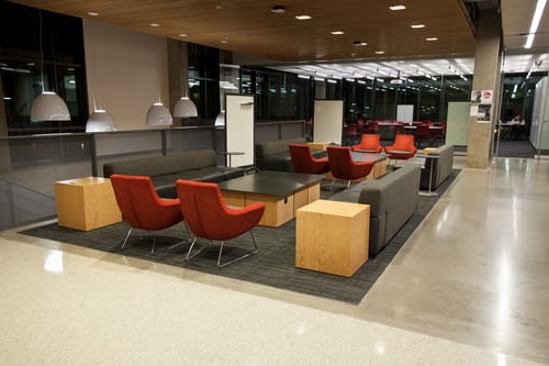 Lobby with multiple gray couches, orange cloth chairs, tables, and large rolling whiteboards. 