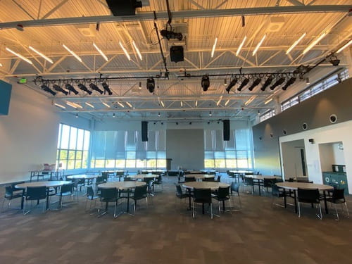 Large open event space filled with many circular group tables and chairs. Floor to ceiling windows along far side of the wall.