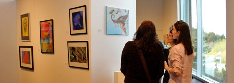 Three people admiring the colorful artwork hung up on the wall.