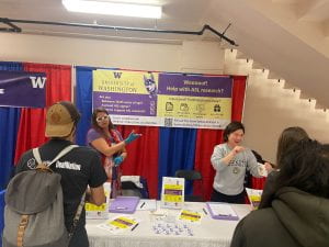 two researchers talking to people in ASL before a purple and yellow banner