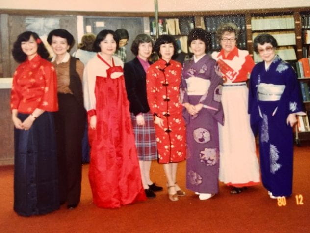 Yeen-mei Wu in a red traditional Chinese dress with seven colleagues, some of whom also wear traditional dress from various countries, at a Library Staff Association Christmas party, 1980.