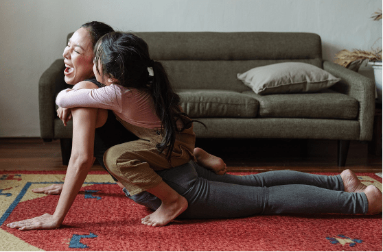 Woman doing yoga pose with young child hugging her