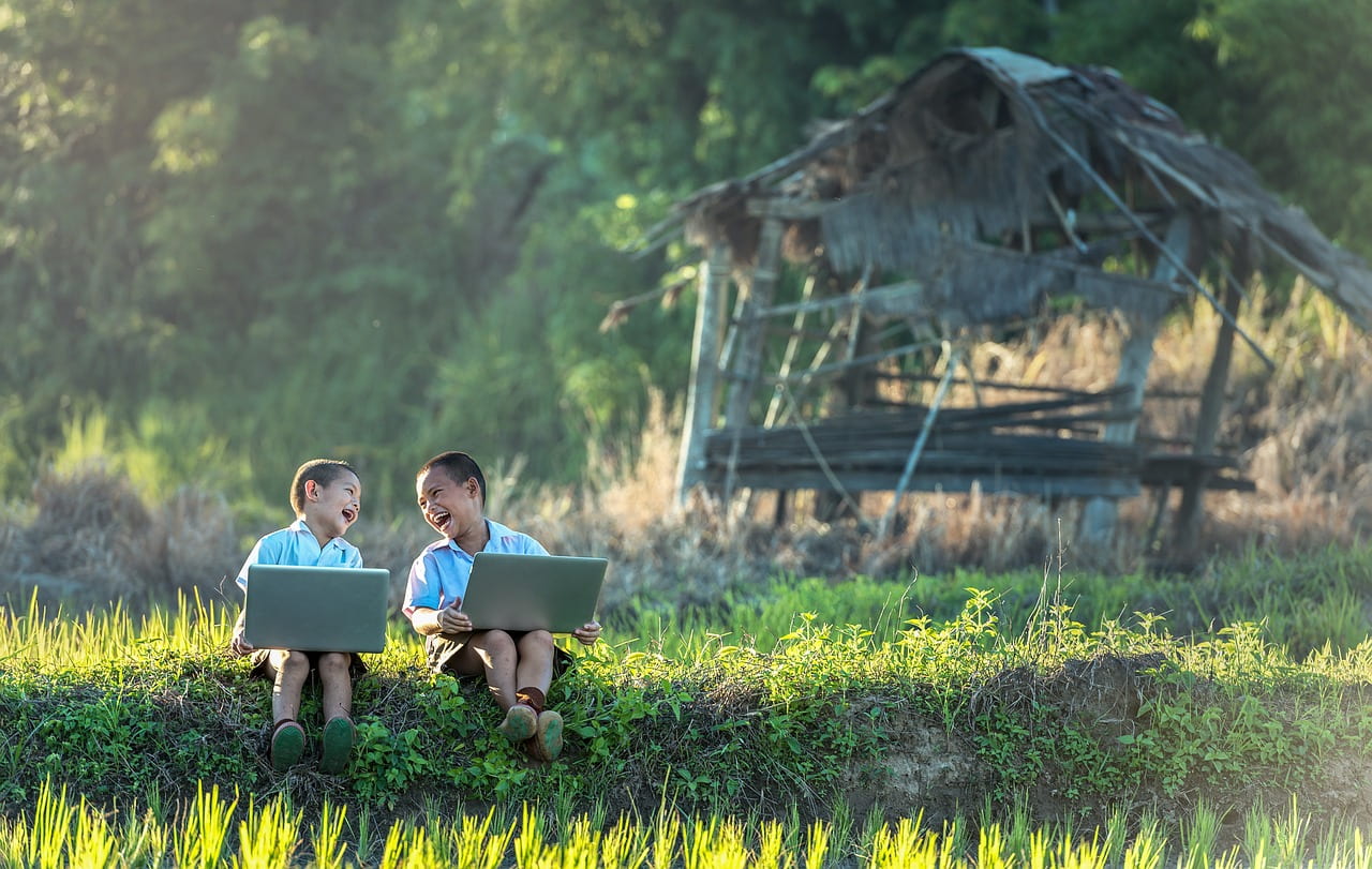 Two young boys sitting outside with laptops