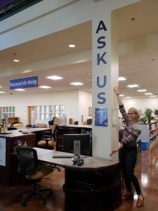 Image of desk in Snoqualmie Building, with Ask Us on the wall, a librarian, and the research help sign.