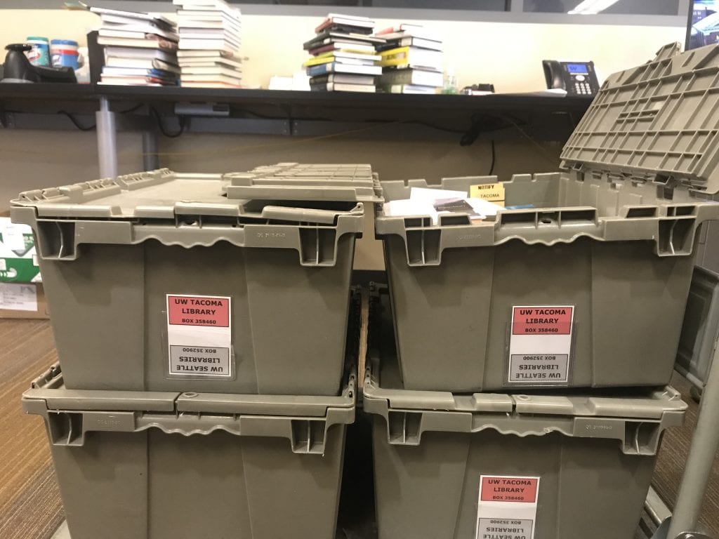 Photo of four grey bins stacked, filled with books ("incoming mail")