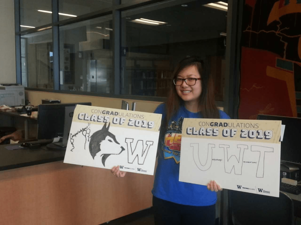 Student holding 2 "conGRADuations Class of 2019" signs, one with UW Husky logo and the other with U W T in block lettering