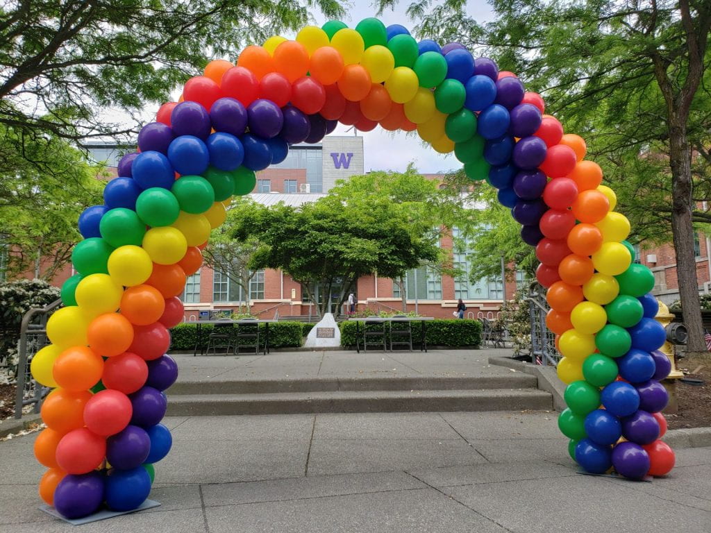 An arch made of rainbow balloons frames the area in front of the Snoqualmie Building and the purple "W" on the Tioga Library Building in the background
