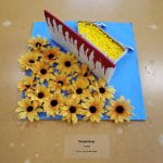 Yellow flowers, a bloody barrier, and yellow beads in a paper boat