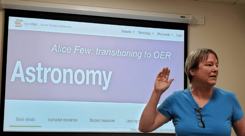 A person raises their right hand while speaking in front of a screen with the title "Alice Few: transitioning to OER: Astronomy"