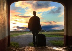 A silhouette of a person holding a suitcase, facing a sunrise.