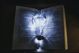 A glowing light bulb in the dark illuminating the pages of a book.