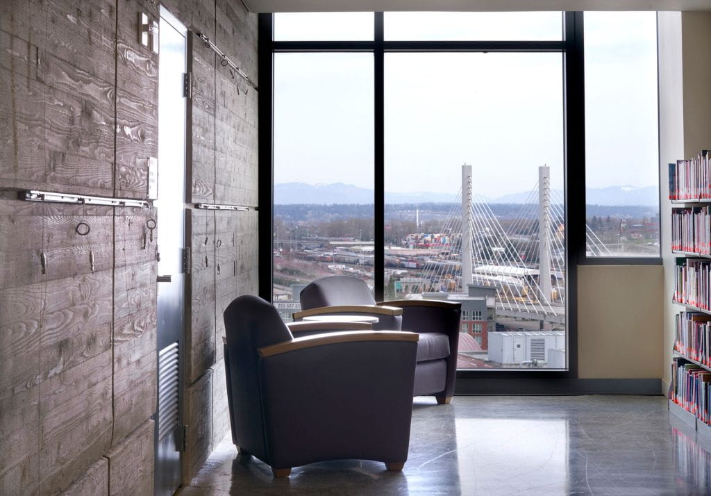Cozy chair against cement wall with floor to ceiling windows overlooking downtown Tacoma