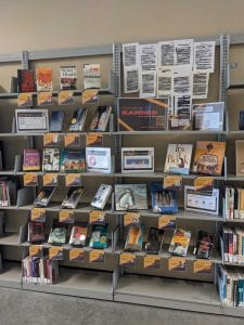 Six rows of books with their covers facing the viewer. Each book is accompanied by a shelf talker detailing why each book has been banned or challenged. Towards the upper right of the display is a large sign that says "These books are banned... But not at this library! Read a banned book today!"