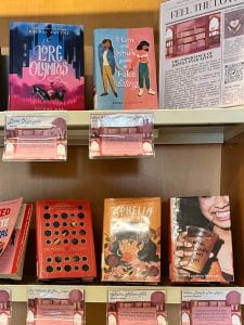 Close up of books included in the Romance display. Mostly pinks, oranges, and reds the titles are Lore Olympus, Hand & Ishu's Guide to Not Dating, The Wrath and the Dawn, Ophelia After All, and When Dimple Met Rishi.