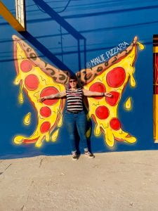 Jessy posed in front of street artwork of two slices of pizza resembling butterfly wings. 