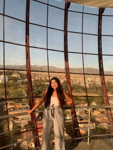 Adrianna standing in front of a wall of windows overlooking Tarija. 